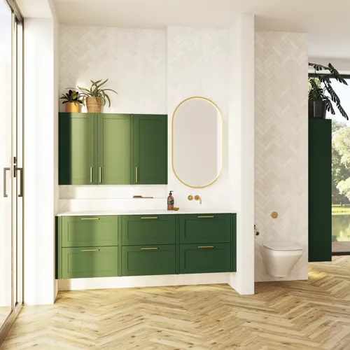 Stort badrum i gröna färger med tvättställsskåp, oval spegel med guldkant och vackra luckor med ram